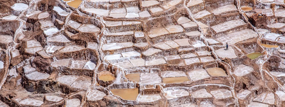 Some of them are still filled with water... Best Hikes In Peru Image: A photograph taken from an elevate view shows a person exploring the salt mines, some of which are still filled with water.