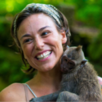 Anywhere Contributor Image: Emma smiles whilst a small monkey clings to her. Her chin length brown hair is held back by a headband.