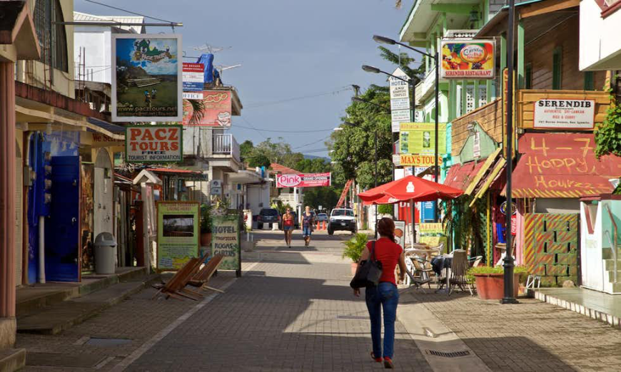 Belize and Guatemala Itinerary Image: A woman walks in denim and a red top carries a black shoulder bag as she walks down a colorful street in San Ignacio.