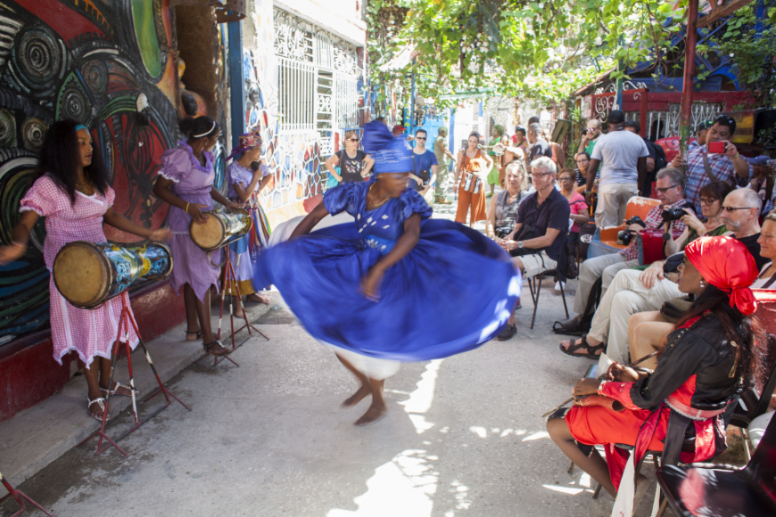 Salsa Dancing in Cuba: Women in colorful dresses play instruments and dance in front of a crowd on a sunny day.